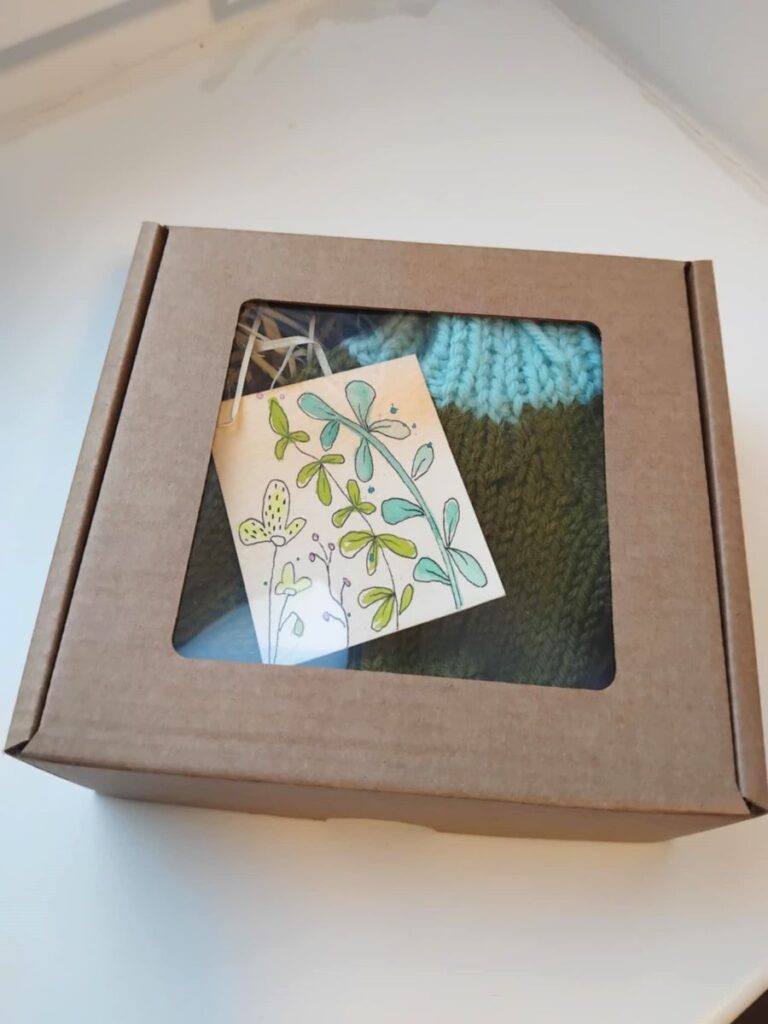 Papist karp, mille sees on käsitööna valminud kootud sokid ning kaunistuseks käsitsi joonistatud taimemotiiviga silt.