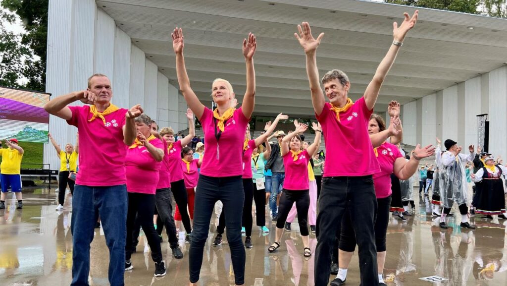 Roosades t-särkides rühm inimesi tantsivad laulukaare all.