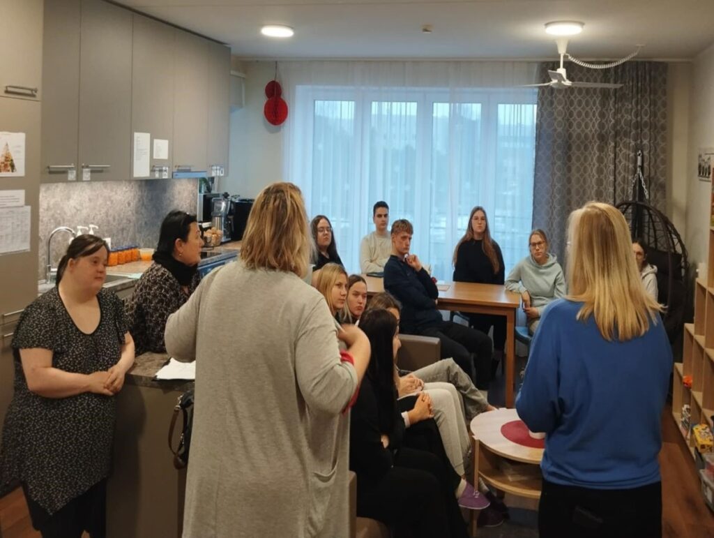 Grup inimesi kuulab toas esitlust, mõned istuvad ja mõned seisavad.