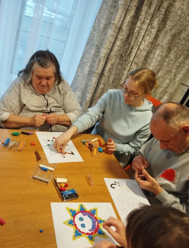 Grup inimest töötab koos laua taga, kasutades plastiliini värviliste mustrite loomiseks paberile.