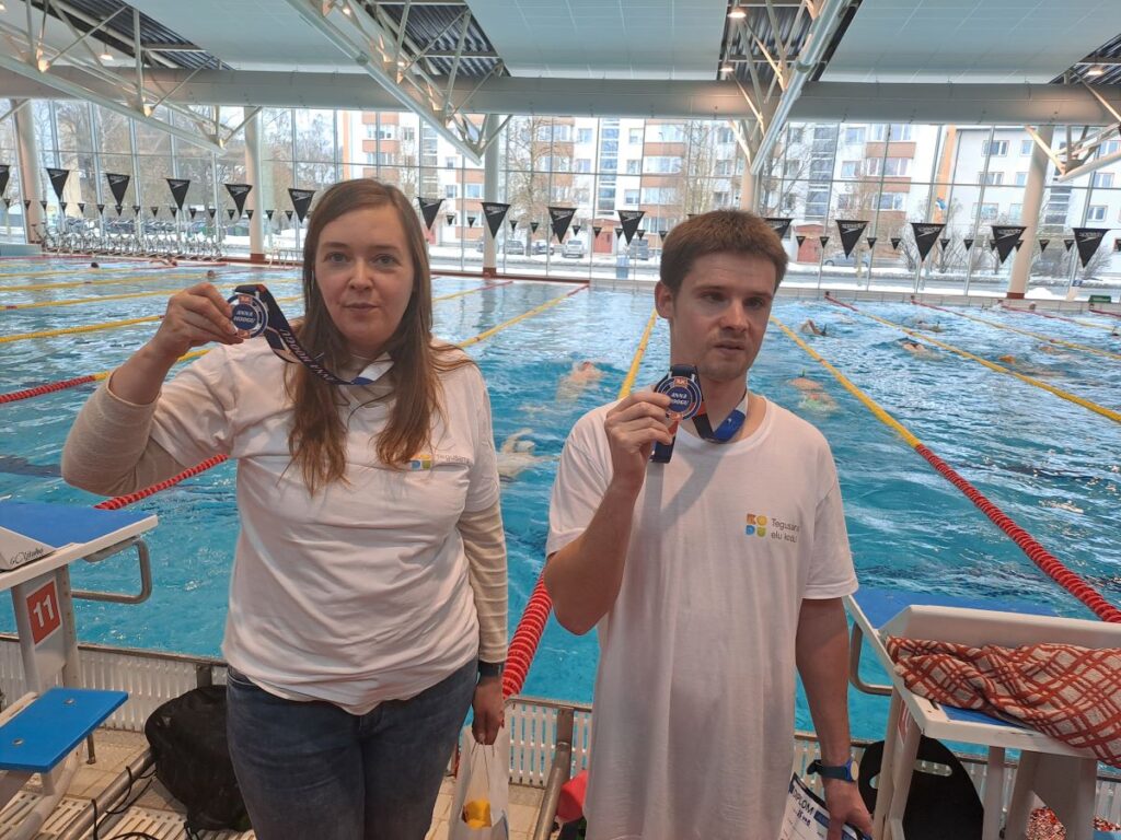 Kaks sportlast seisavad Aura Veekeskuse basseini ääres, hoides uhkelt käes oma võistlusmedaleid.