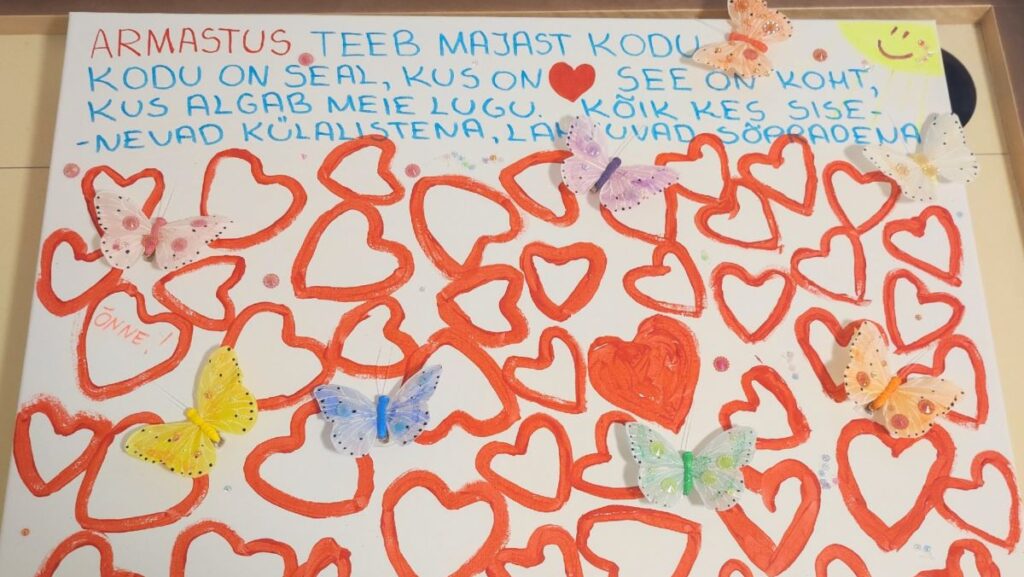 PIlt südamekujundite ja värviliste liblikatega. Üleval on kirjutatud tekst armastuse ja kodu tähendusest.