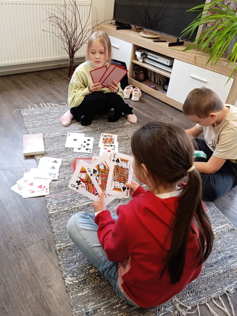 3 last istuvad põrandal maas ja mängivad kaardimängu. 