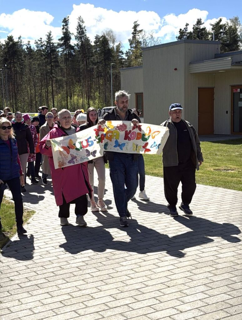 Uus-Sauga Kodu inimesed rongkäigus, ees värvikas silt liblikatega.