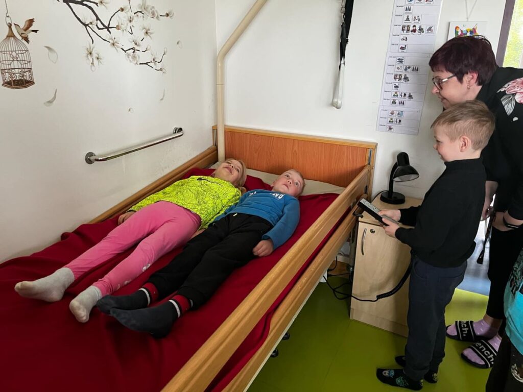 Kaks last lamavad hooldusvoodis, üks laps proovib voodi puldiga selle asendit muuta, kõrval jälgib täiskasvanu.