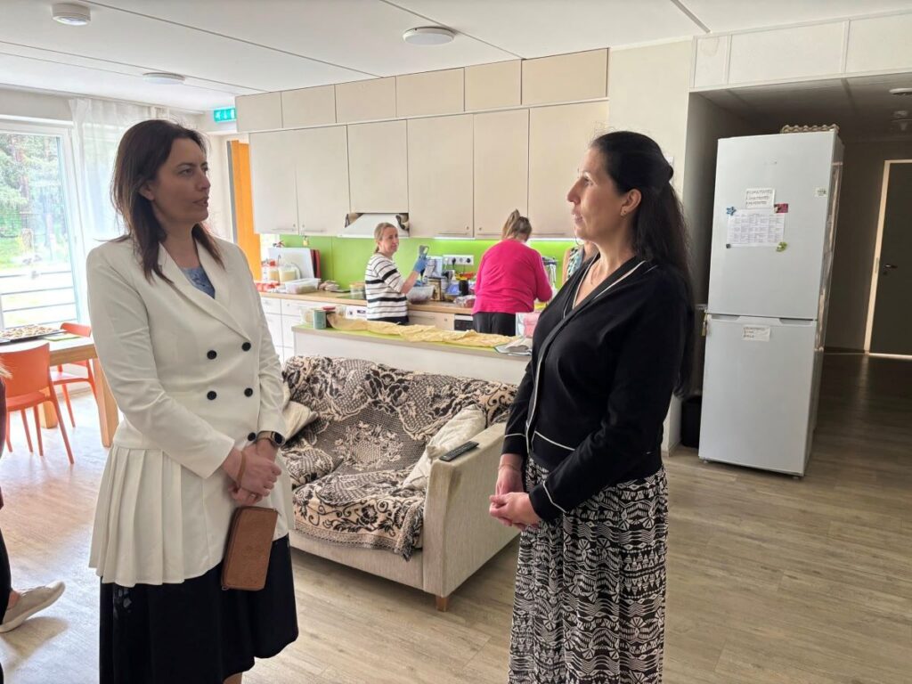 Sotsiaalminister Karmen Joller ja Inge Kändla vestlevad Mustamäe kodu köögialal, taustal valmivad kohvikupäeva ettevalmistused.