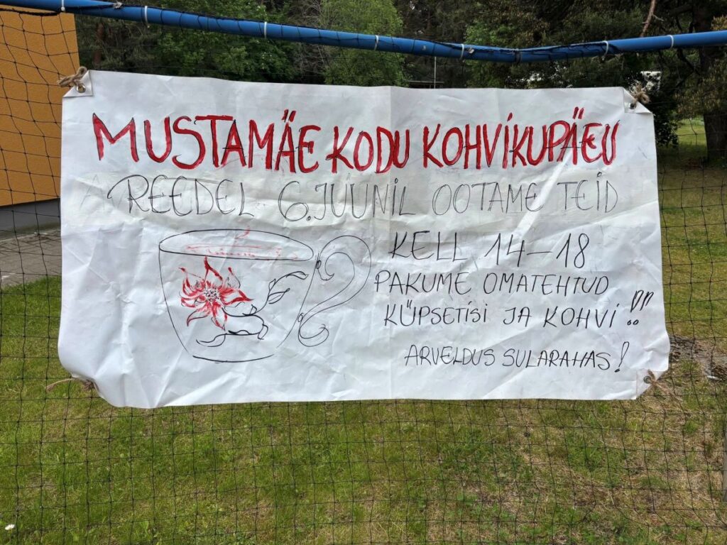 Käsitsi joonistatud plakat Mustamäe kodu kohvikupäevast, kinnitatud jalgpallivärava külge – info ürituse aja ja sisu kohta