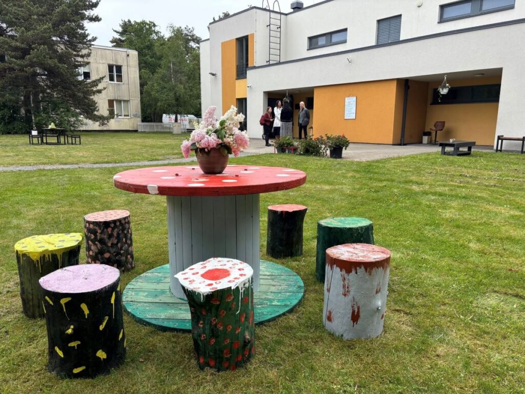 Mustamäe kodu hoov, ees värviliste kändudega kaunistatud laud ja pinkide komplekt, taustal hoone ja inimese