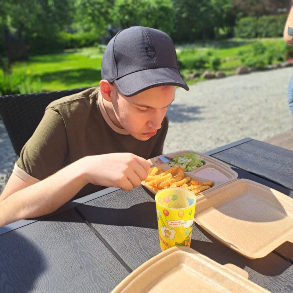 Noormees sööb plastkarbist friikartuleid ja salatit, istudes päikselise ilmaga õues laua taga.