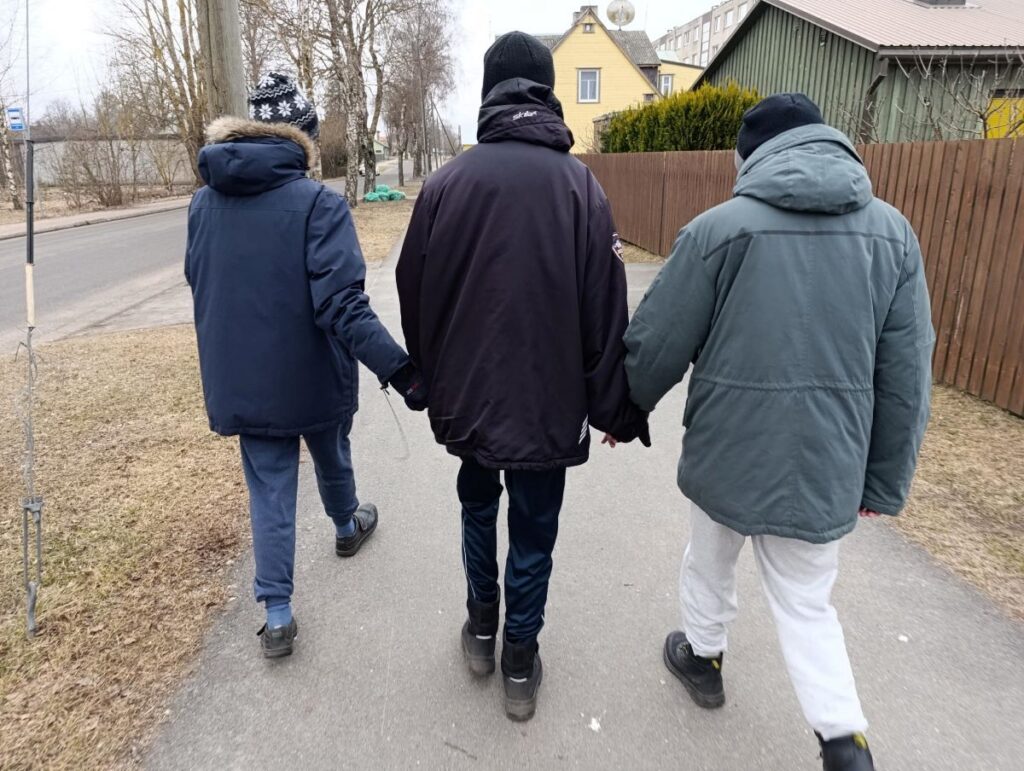 Kolm inimest jalutavad käsikäes kõnniteel, seljas soojad joped ja peas mütsid.