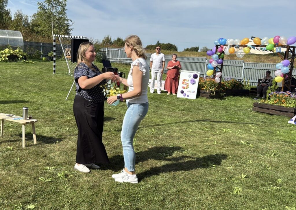 Üks naine annab teisele naisele üle lilleampli tänutäheks. 