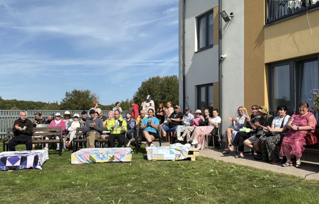 Ahtme Salu kodu 5. sünnipäeva külalised ja kodu elanikud istuvad õues pinkidel ja aplodeerivad.