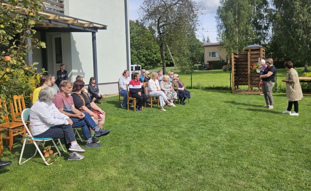 Külastajad ja elanikud istuvad toolidel Jõgeva Allika kodu hoovis kuulates piirkonnajuht Imbi Regot.