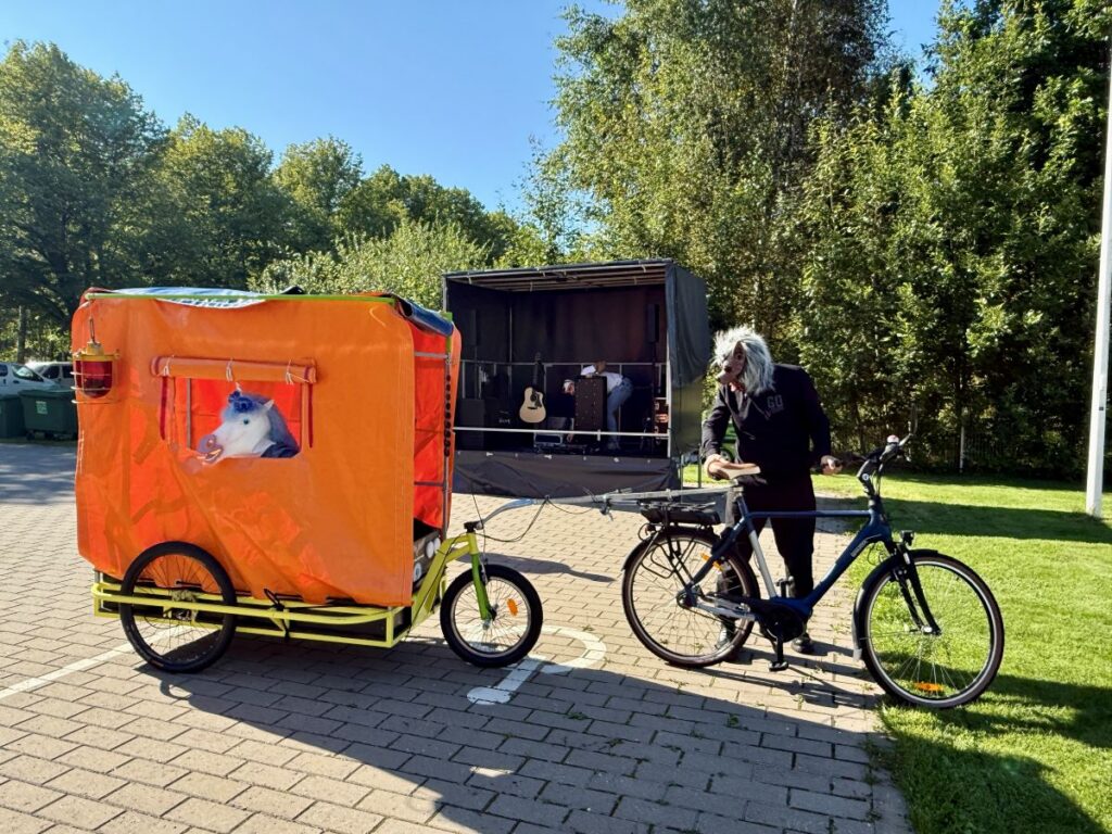 Hundi maskiga mees on jalgratta juures ja erkoranzis kärus ratta taga istub ükssarviku maskiga naine. 