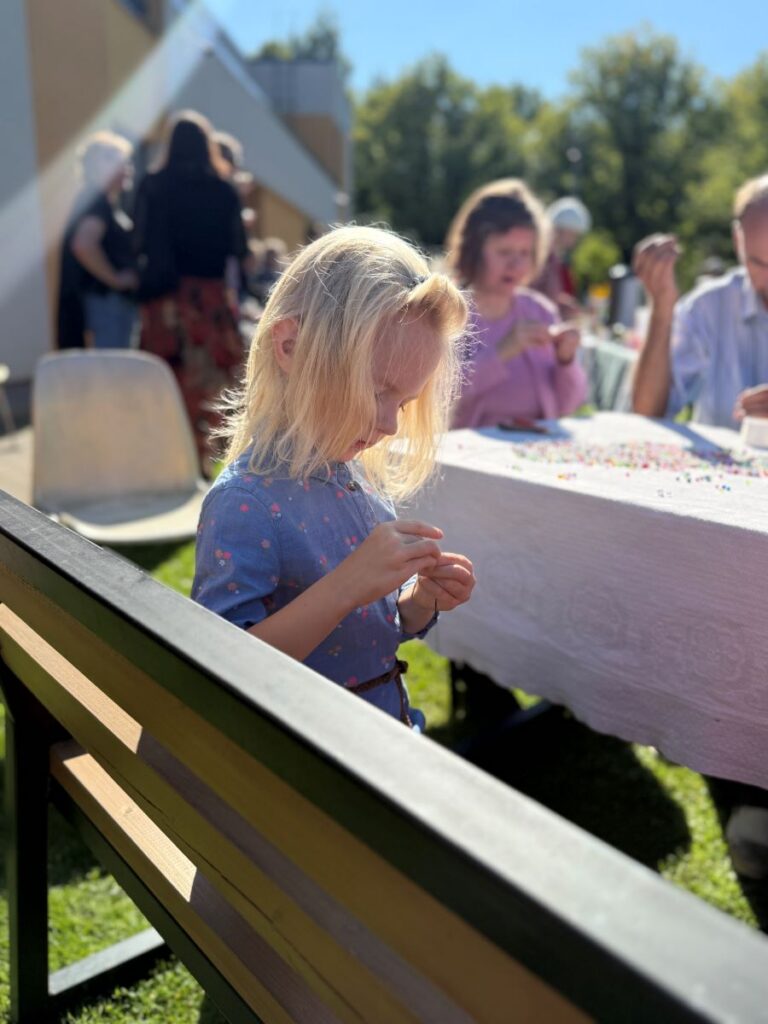 Väike tüdruk istub päikselisel pingil ja valmistab käevõru käsitöölauas.
