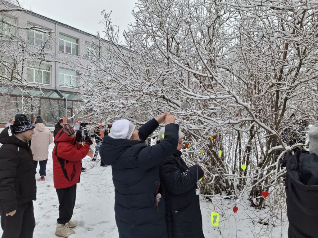 Sinimäe ja Sillamäe kodu elanikud riputavad talvises lumes helkureid Sillamäe raamatukogu juures kasvavatele puudele.