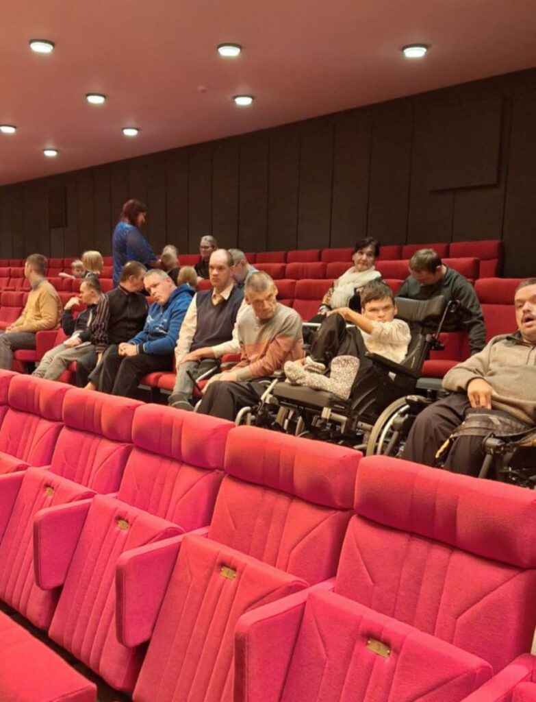 Inimesed istuvad punastes toolides ja ka ratastoolides kinosaalis, ootamas seansi algust.