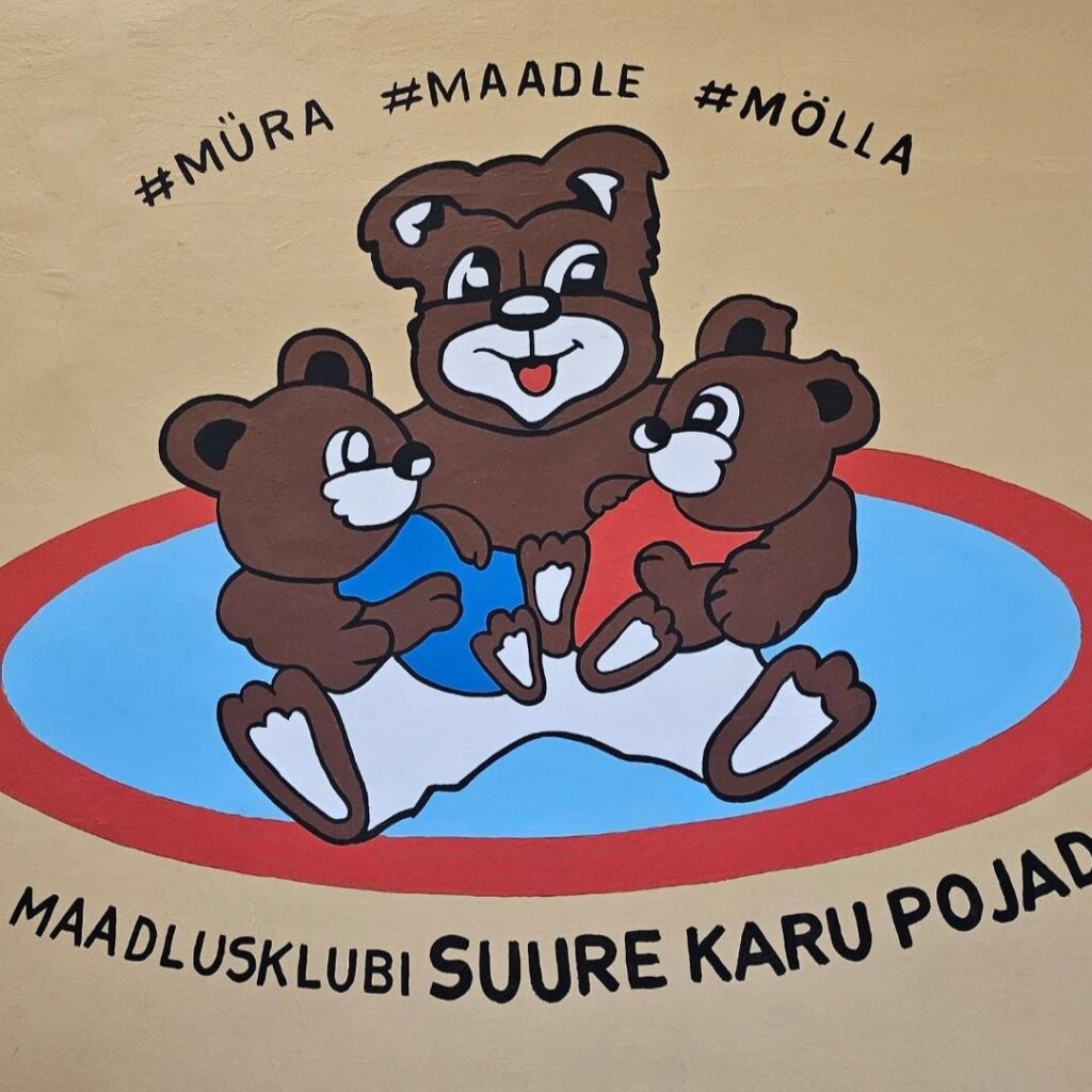 Maadlusklubi Suure Karu Pojad logi, kus maadlusmatil istub suur karu, kelle süles 2 väikest karu. 