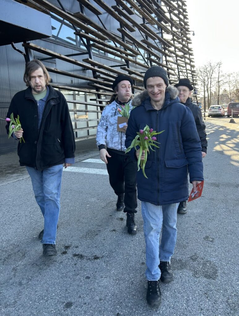 Neli meest kõnnivad õues, käes tulbid ja õnnitluskaardid.