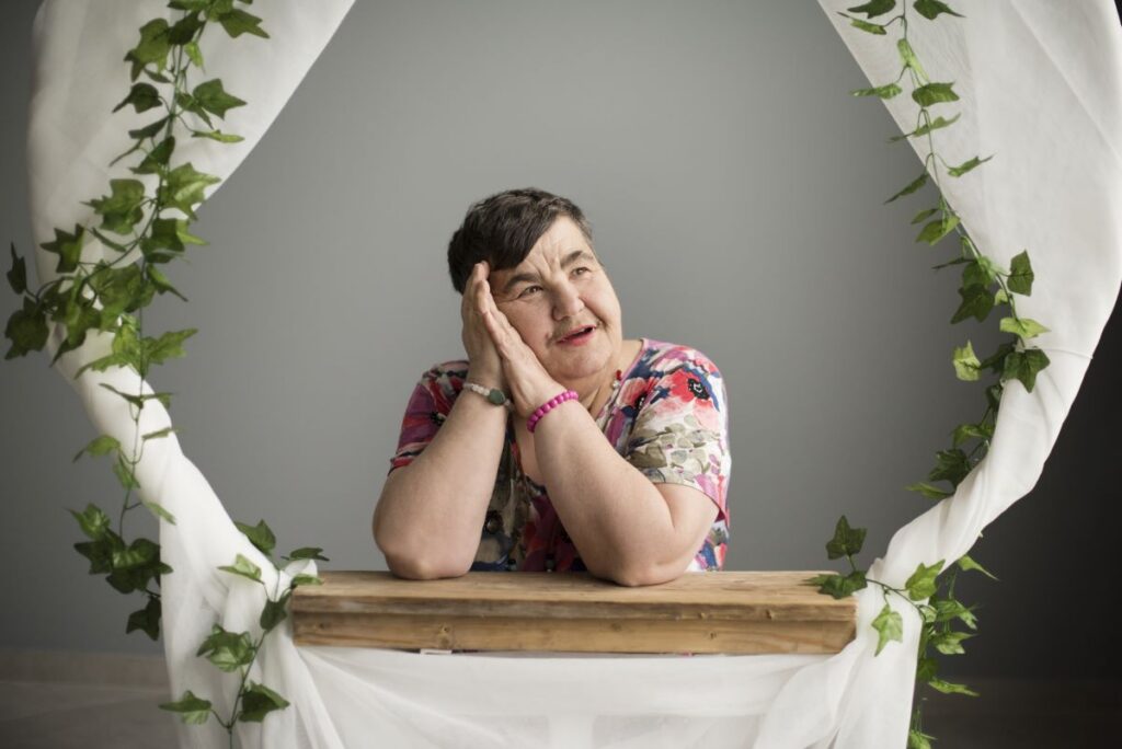 Naine poseerib lillede ja valge kangaga kaunistatud tausta ees.