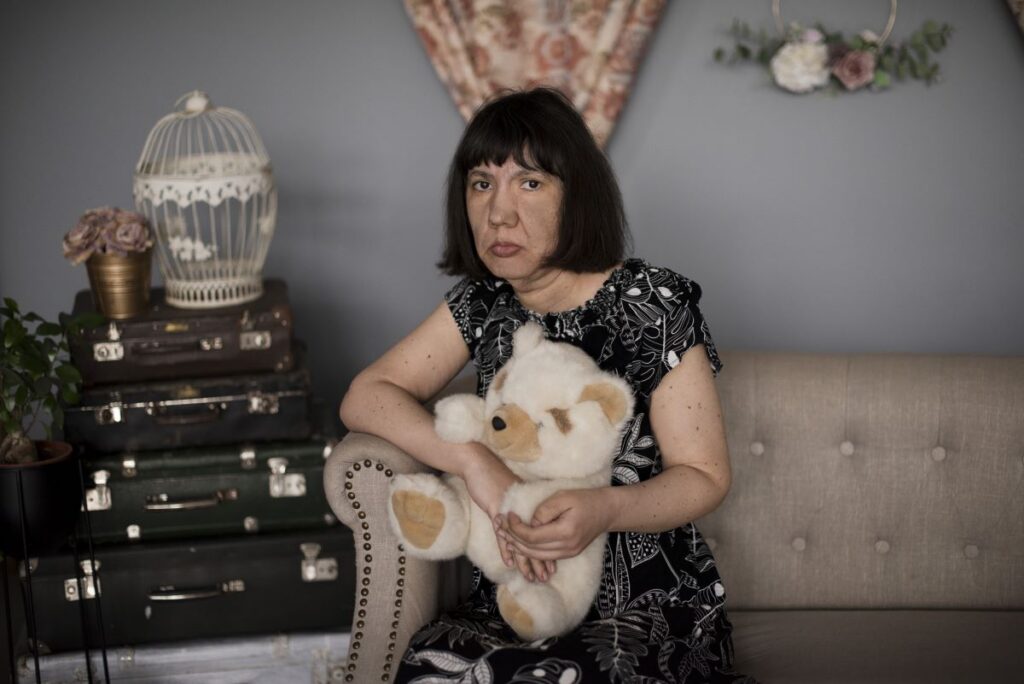 Naine istub fotostuudios diivanil ja hoiab kaisukaru.