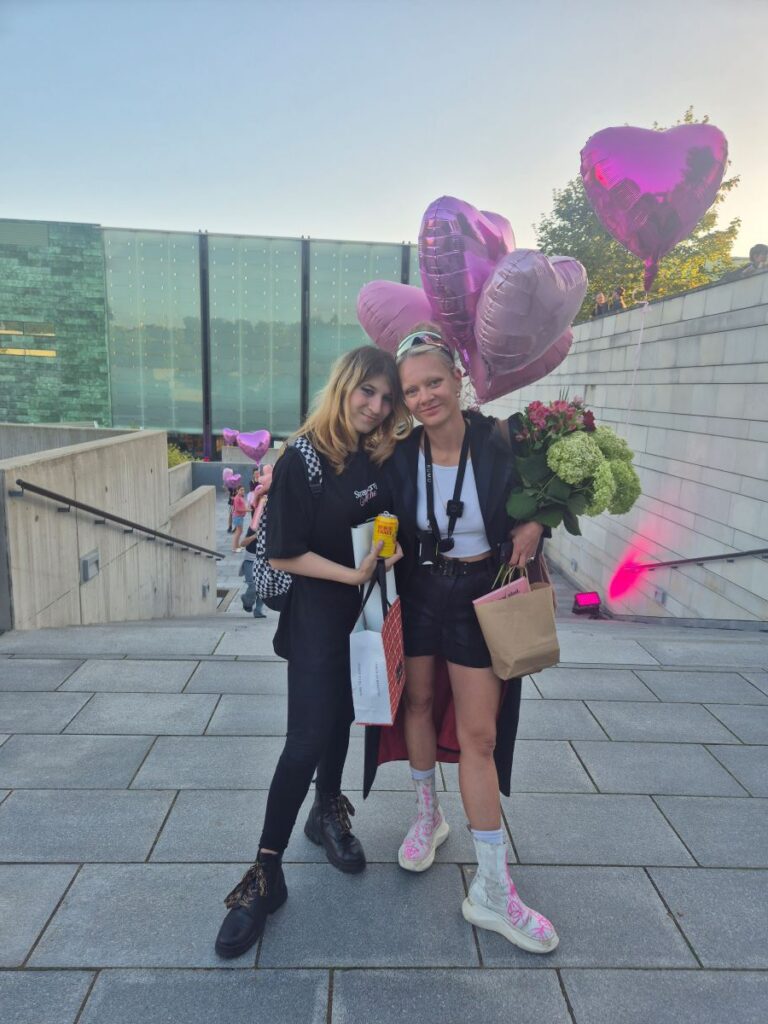 Karina ja Marta Vaarik poseerivad. Martal on käes õhupallid ja lilled.